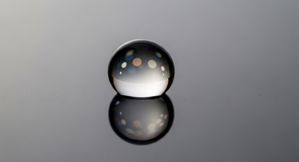 Abstract, minimalist photo of a reflective black and clear sphere on a glossy gray surface, symbolizing a fragrance molecule like Iso E Super or Cetalox.