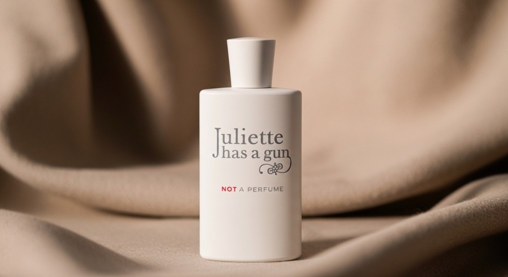 Close-up of the square, matte white Juliette Has a Gun Not a Perfume bottle, set against a background of warm, draped beige fabric.