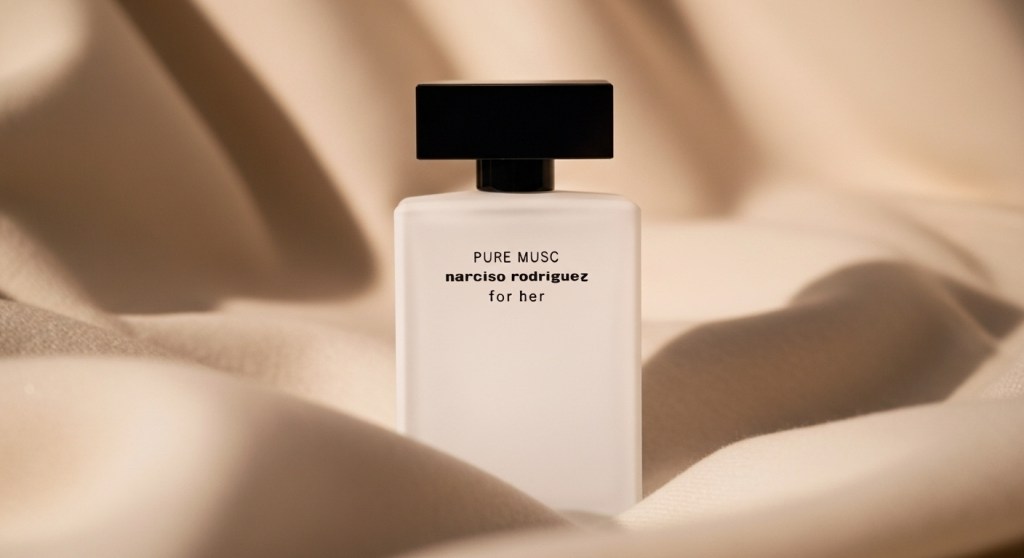 Close-up of the matte white Narciso Rodriguez For Her Pure Musc bottle with a black cap, set against a background of warm, flowing beige fabric.